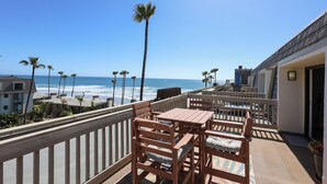 Een balkon met houten meubels, uitzicht op de oceaan en palmbomen.