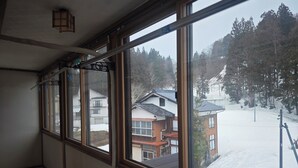 A room with large windows, a wooden floor, and a view of a snowy landscape with buildings. - A whole building of a Showa-era mansion for rent｜11 persons per day per couple, 4-minute drive to one of Japan's top 3 medicinal hot springs, 4 hot spring tours in the area, pet dogs OK, terraced rice paddies and 4-meter snow-covered mountain village, tot (十日町市)