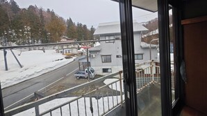 Blick vom Balkon mit Metallgeländer, eine verschneite Straße und ein Gebäude mit weißer Fassade.
