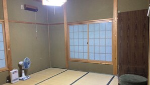 Ein Raum mit Tatami-Matten, einer Schiebetür, einem Standventilator, einer Heizung und einem Futon.