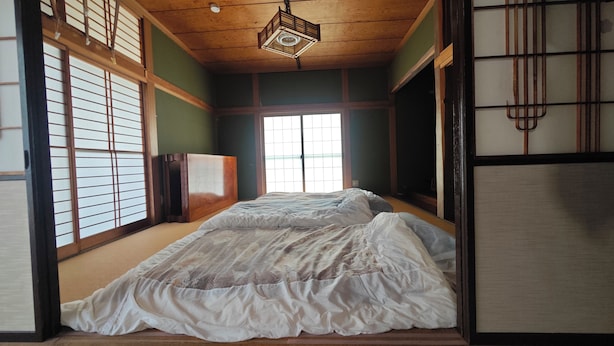 Ein traditioneller japanischer Raum mit Tatami-Böden, Schiebetüren und einem Bett mit weißer Bettdecke.