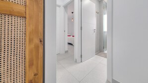 Un pasillo que da a una habitación con cama, una puerta con panel de vidrio y una lámpara en el techo.