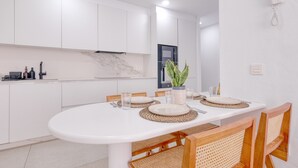 Una cocina moderna con armarios blancos, salpicadero de mármol y comedor con una mesa blanca dispuesta para cuatro.