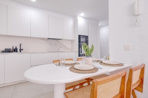 A modern kitchen with white cabinets, a marble backsplash, and a dining area with a white table set for four. - Casa Nubea • 500M from the beach • LVH (La Santa)