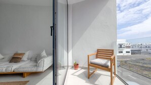 Un balcón con un sofá, una silla de madera y plantas en macetas.