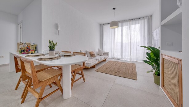 Una sala de estar moderna con una mesa de comedor, sillas, un sofá, un ventanal con cortinas y una planta en maceta.