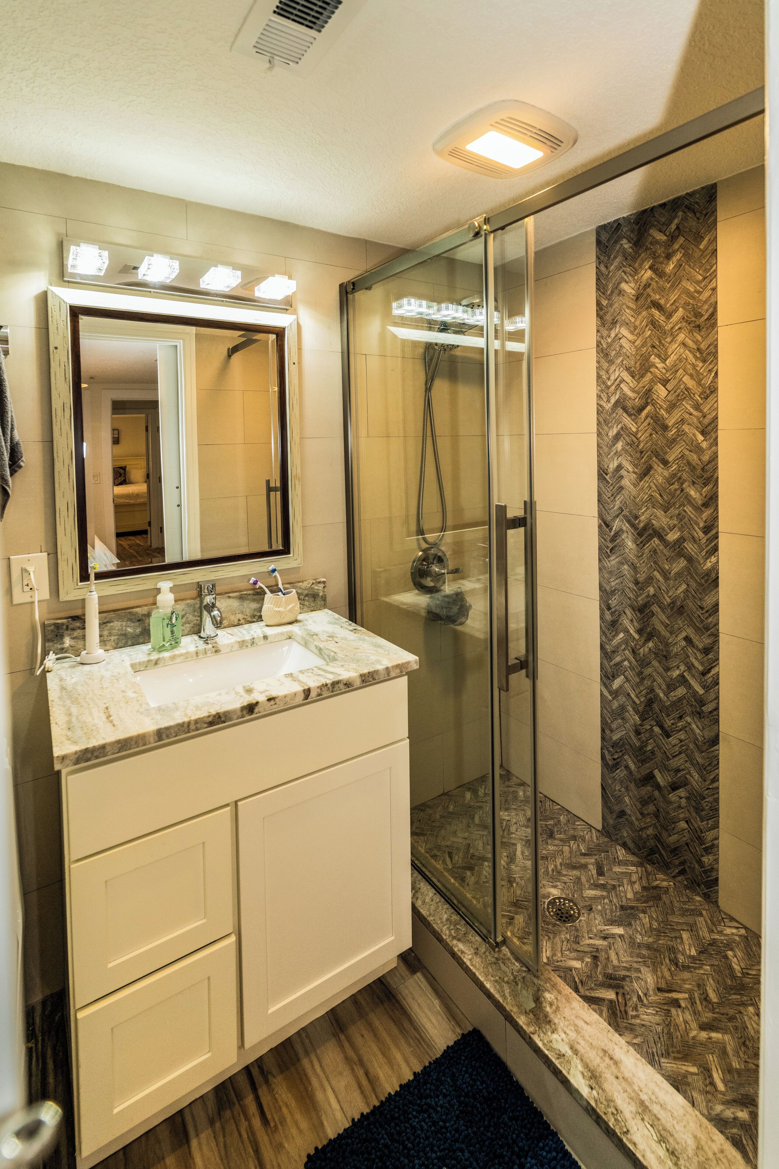 A bathroom with a glass shower enclosure, a vanity with a mirror, and a herringbone-patterned wall.