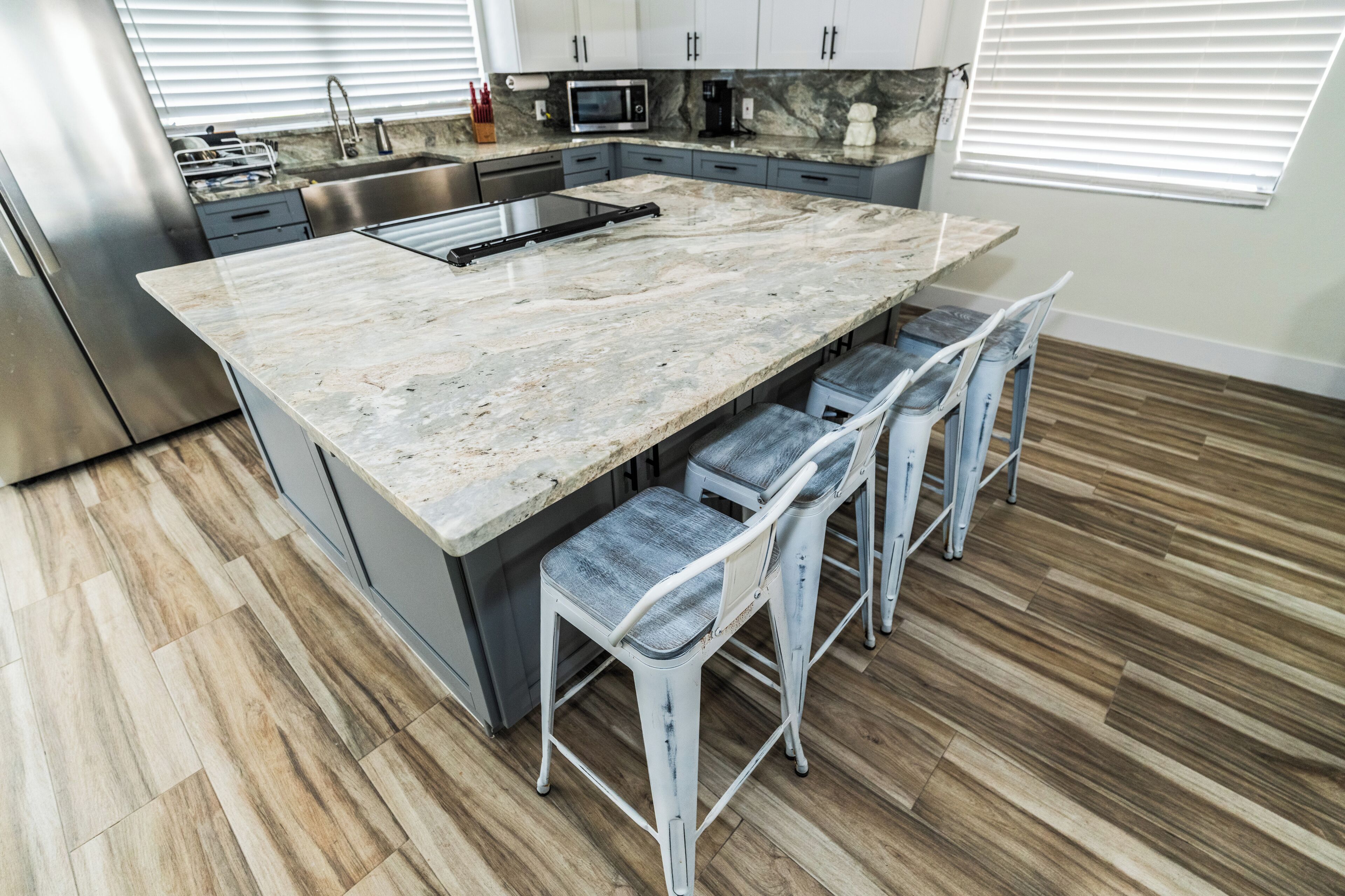 A kitchen with a marble island, stainless steel appliances, and wooden flooring.