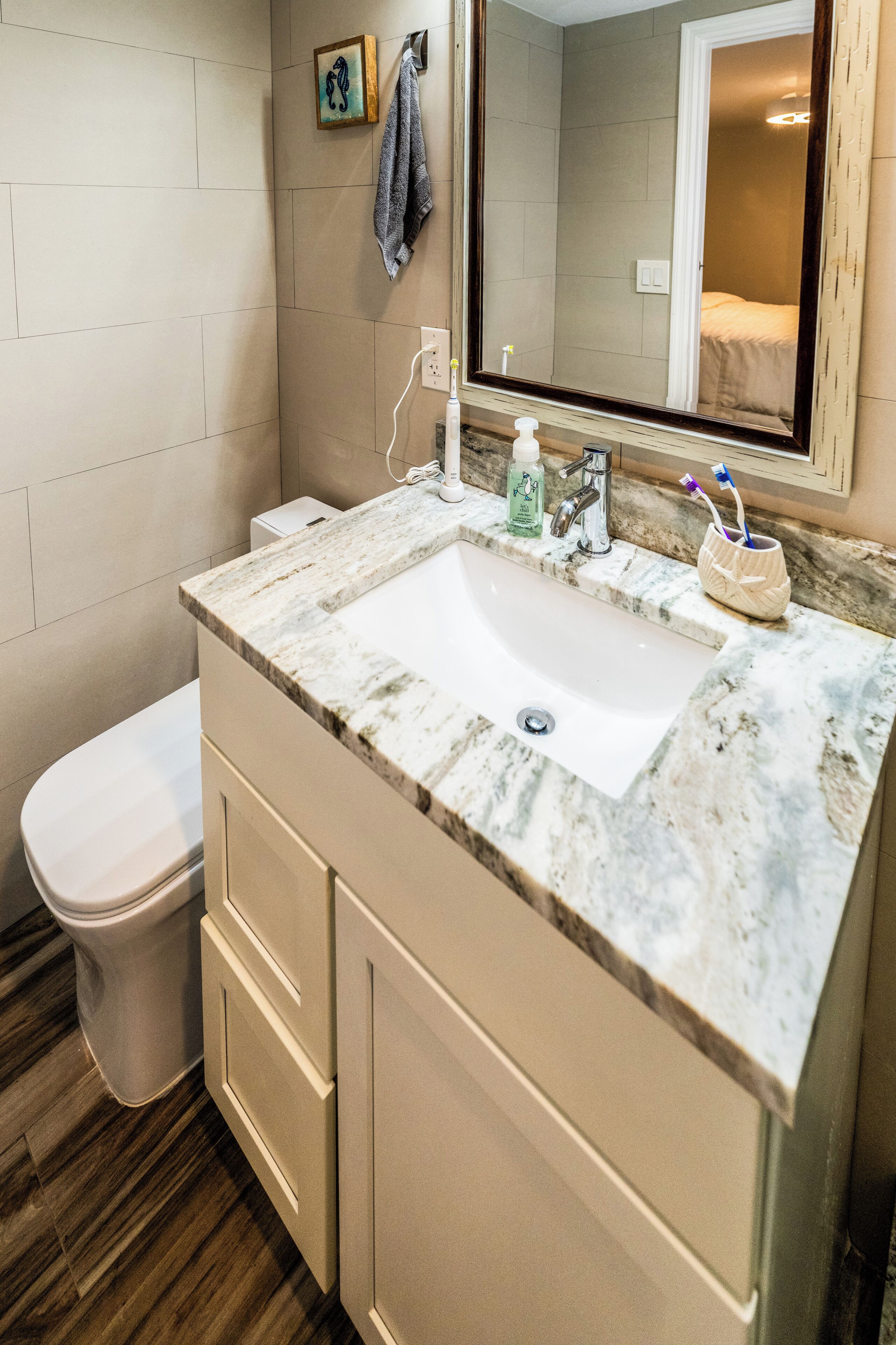 A bathroom with a marble sink, a toilet, and a mirror reflecting a bed.