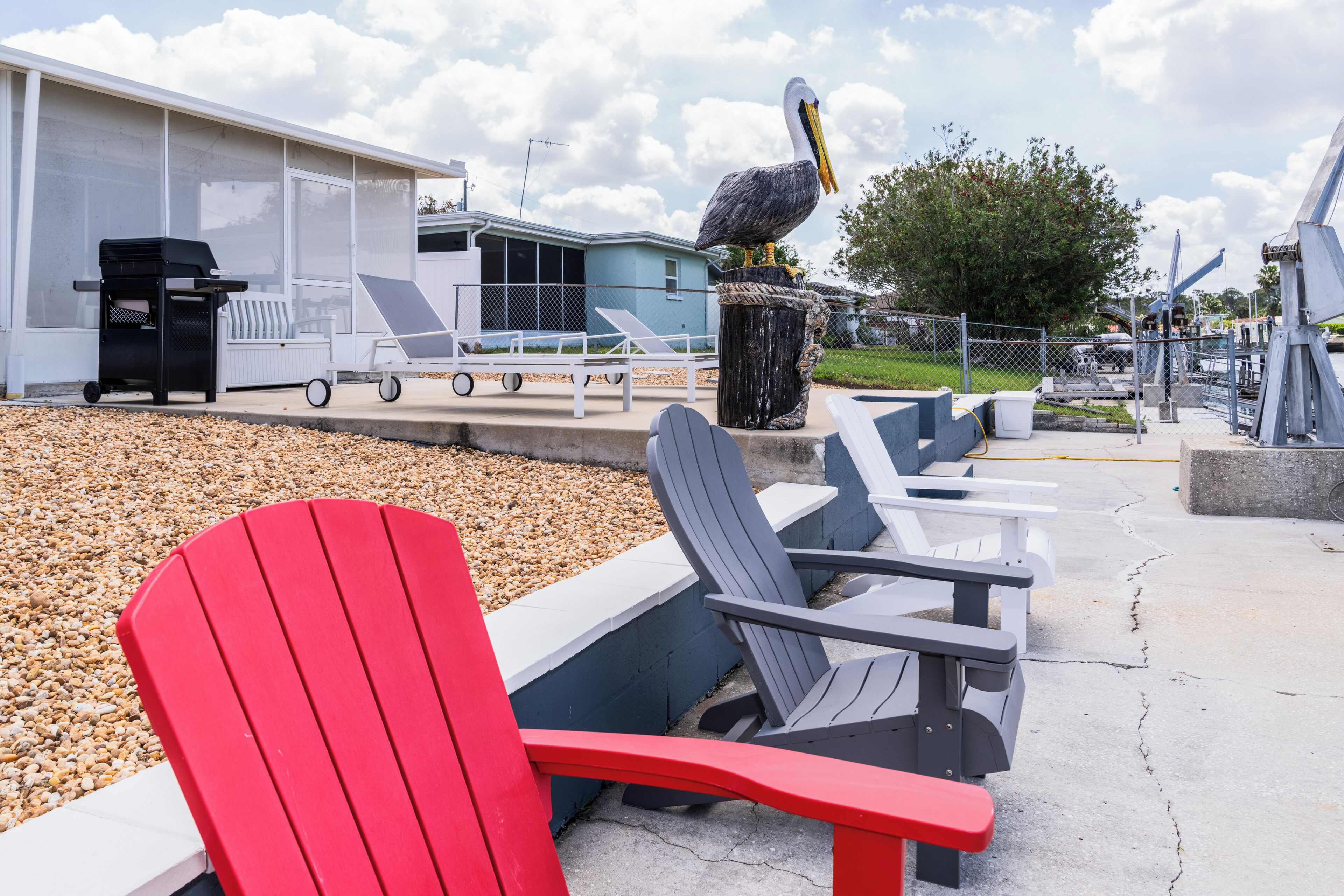 Espace extérieur aménag é avec des chaises Adirondack, une statue de pélican et un bâtiment doté d’une zone abritée.