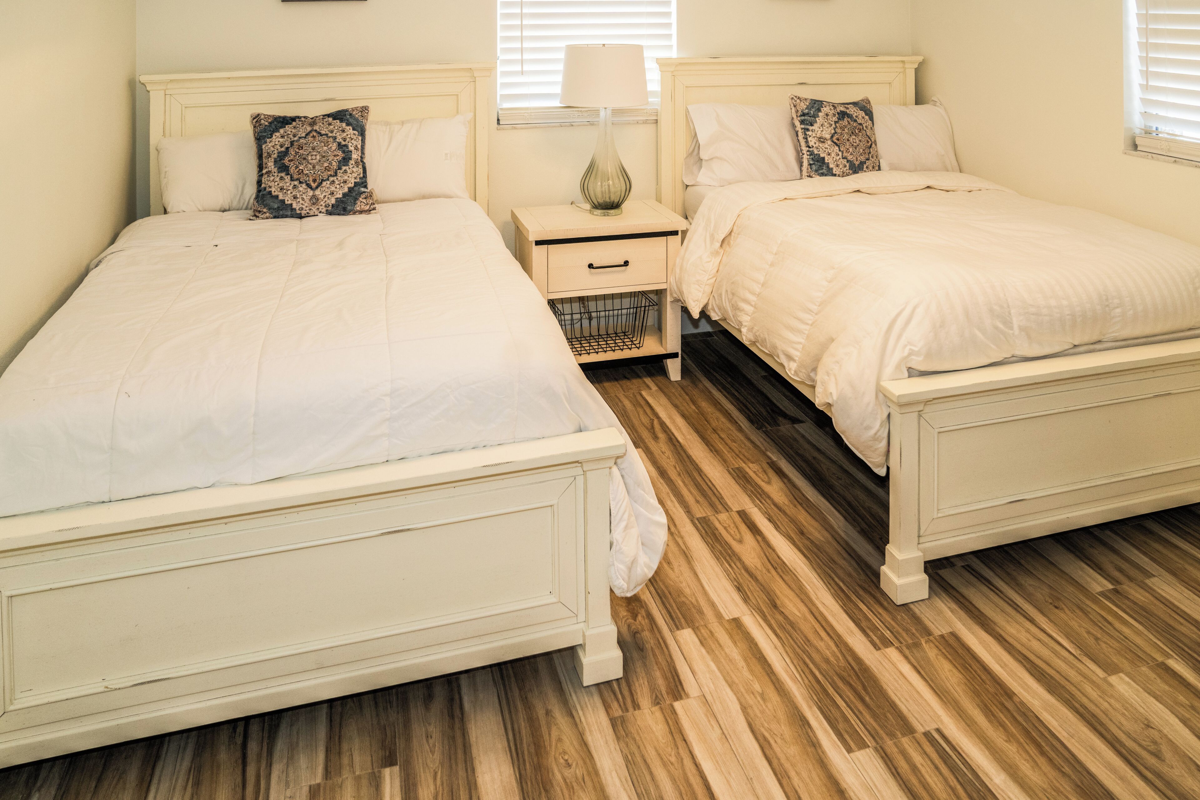 A bedroom with two beds, a nightstand, and a lamp.