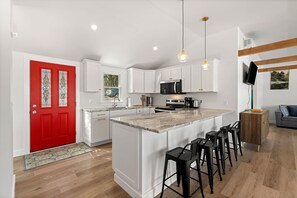 A modern kitchen with white cabinetry, a red door, and a bar area with stools.