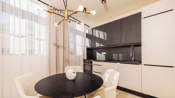 Una cocina moderna con encimera negra, armarios blancos y un comedor con mesa redonda y sillas.