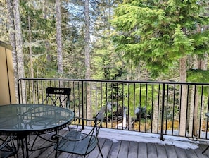 Eine Terrasse mit rundem Tisch und Stühlen, umgeben von einem Metallgeländer, mit Blick auf ein bewaldetes Gebiet.