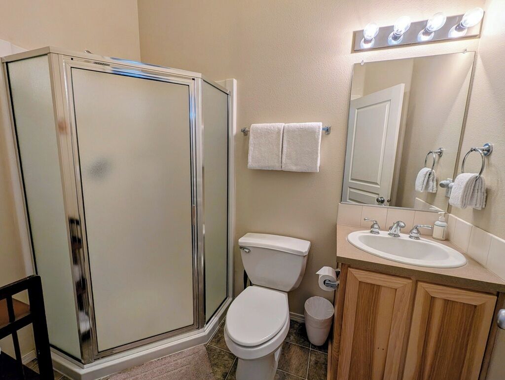 Un baño con cabina de ducha de vidrio, inodoro, lavamanos con espejo y barra para toallas.