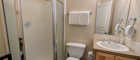Un baño con cabina de ducha de vidrio, inodoro, lavamanos con espejo y barra para toallas.