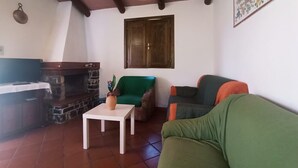 Uma sala de estar com lareira de pedra, televisão, poltrona verde, sofá e mesa branca.