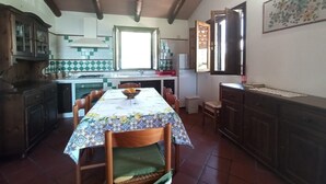 Uma cozinha com mesa, cadeiras, armários, uma janela e um objeto decorativo na parede.