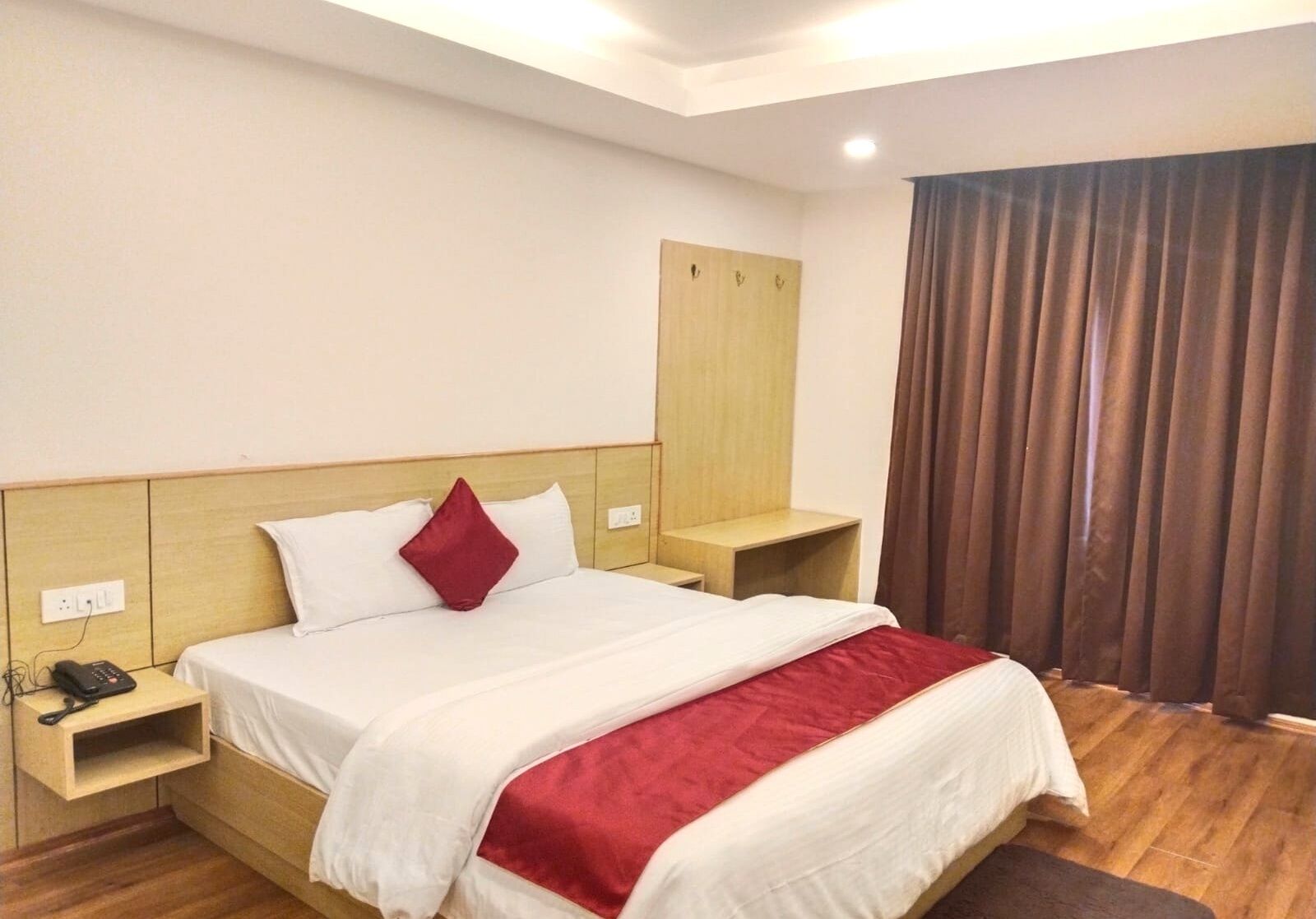 Una habitación de hotel con cama, mesitas de noche, teléfono, armario y ventana con cortinas.