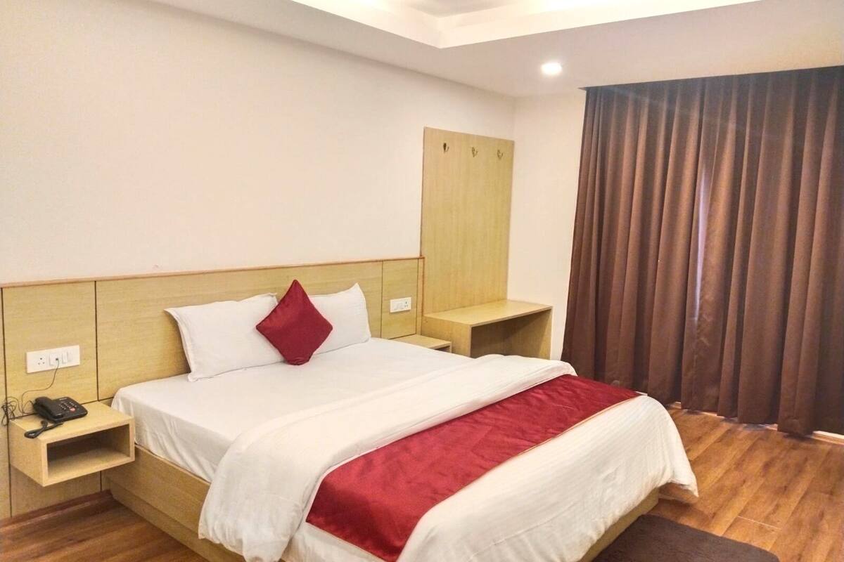 A hotel room with a bed, bedside tables, a telephone, a wardrobe, and a window with curtains.