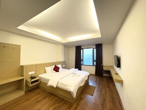 A modern hotel room with a bed, bedside table, built-in TV, and a window with a view. - Swastik Inn beside swastik medical store (Gangtok)