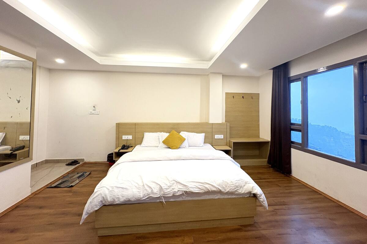 A modern hotel room with a large bed, a bedside table, a mirror, and a window with a view.