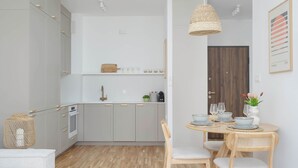 A modern kitchen with grey cabinets, a wooden dining table set for four, and a hanging light fixture. - Modern Apartment | Air Conditioning, Balcony, Underground Parking (Warszawa)