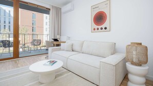 A modern living room with a sofa, a round coffee table, a wicker sculpture, and a Bauhaus poster. - Modern Apartment | Air Conditioning, Balcony, Underground Parking (Warszawa)