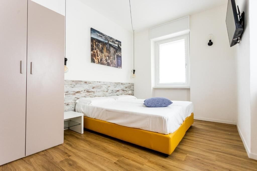 Ein Schlafzimmer mit Bett, Kleiderschrank, Schreibtisch, einem Fenster und einem Stadtbild an der Wand.