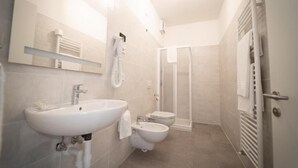 Un baño con lavamanos, bidé, inodoro y cabina de ducha.