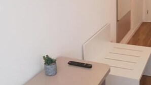 A modern room with a flat-screen TV mounted on the wall, a small potted plant, a remote control, and a white chair.