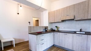 A modern kitchen with light wood cabinets, a dark countertop, and a small white bench.