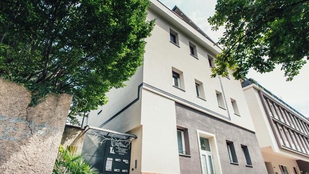 Un edificio de varios pisos con fachada moderna, entrada protegida por una reja y un pequeño jardín.