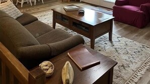 Een woonkamer met een bank, salontafel, eettafel met stoelen en een plafondventilator.