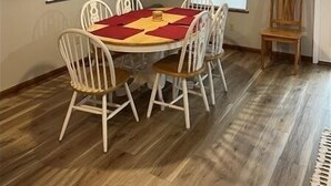 Een eetruimte met een ronde tafel, witte stoelen, een houten vloer en een plafondlamp.