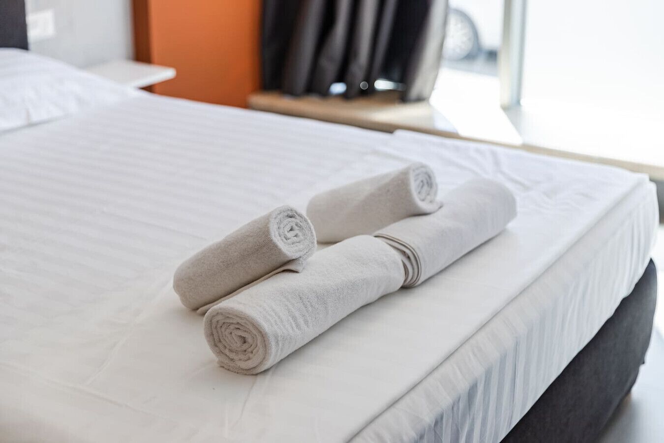 Un lit bien fait, avec deux serviettes enroulées, un matelas blanc et une tête de lit sombre.