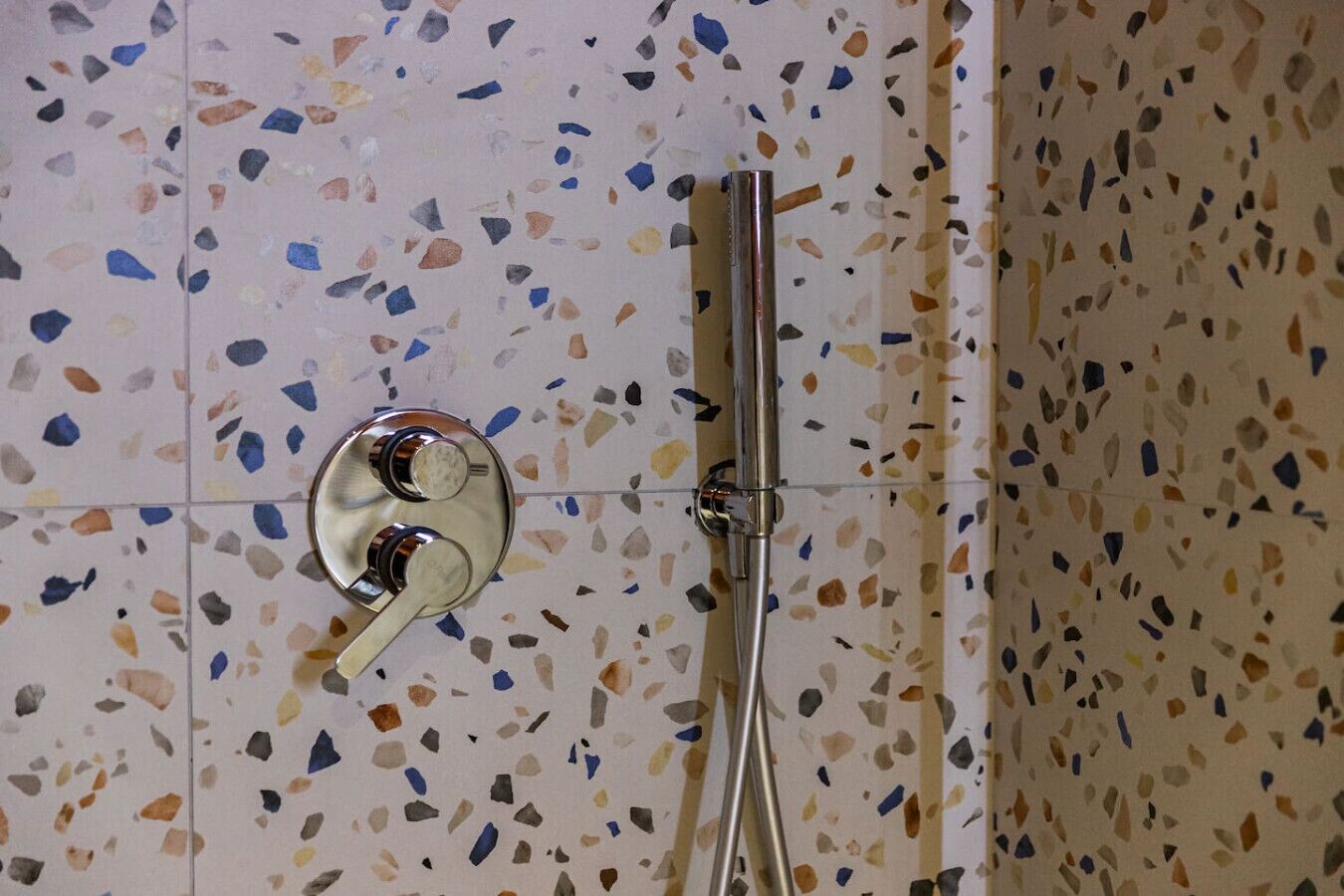 A shower with a chrome faucet and a handheld showerhead, set against a speckled tile wall.