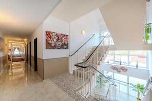 Un interior moderno con un pasillo de suelo de mármol, una escalera con barandillas de metal y una gran obra de arte floral en la pared.
