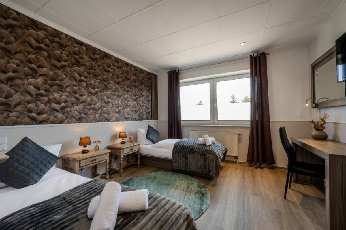 A hotel room with a stone wall, two beds, a desk, and a large window.