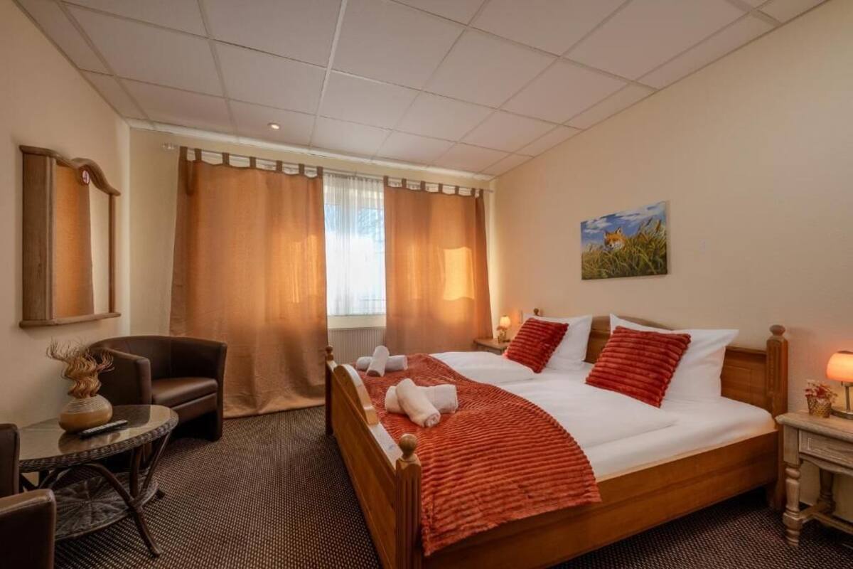 A hotel room with a bed, a chair, a small table, and a painting on the wall.