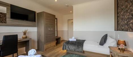 A hotel room with a bed, a desk, a chair, a TV, and a wardrobe.