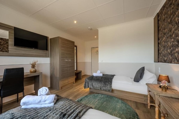 A hotel room with a bed, a desk, a chair, a TV, and a wardrobe.
