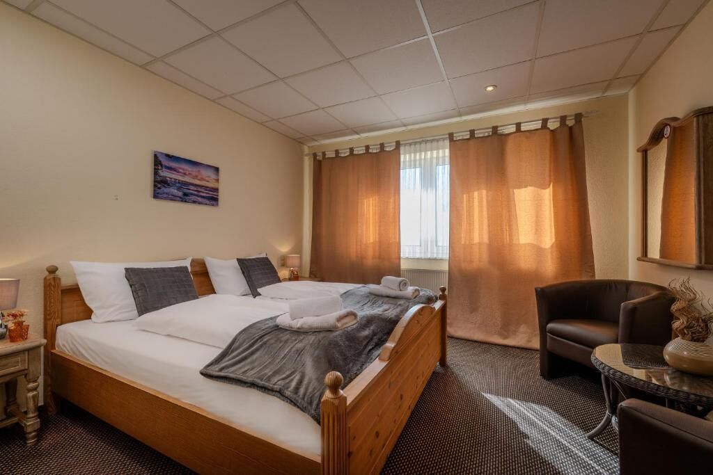 Una habitación de hotel con una cama de madera, una silla, una mesita y una ventana con cortinas.