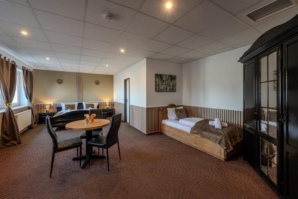 Habitación de hotel con cama, sofá, mesa de comedor con sillas, cocina y un ventanal con cortinas.