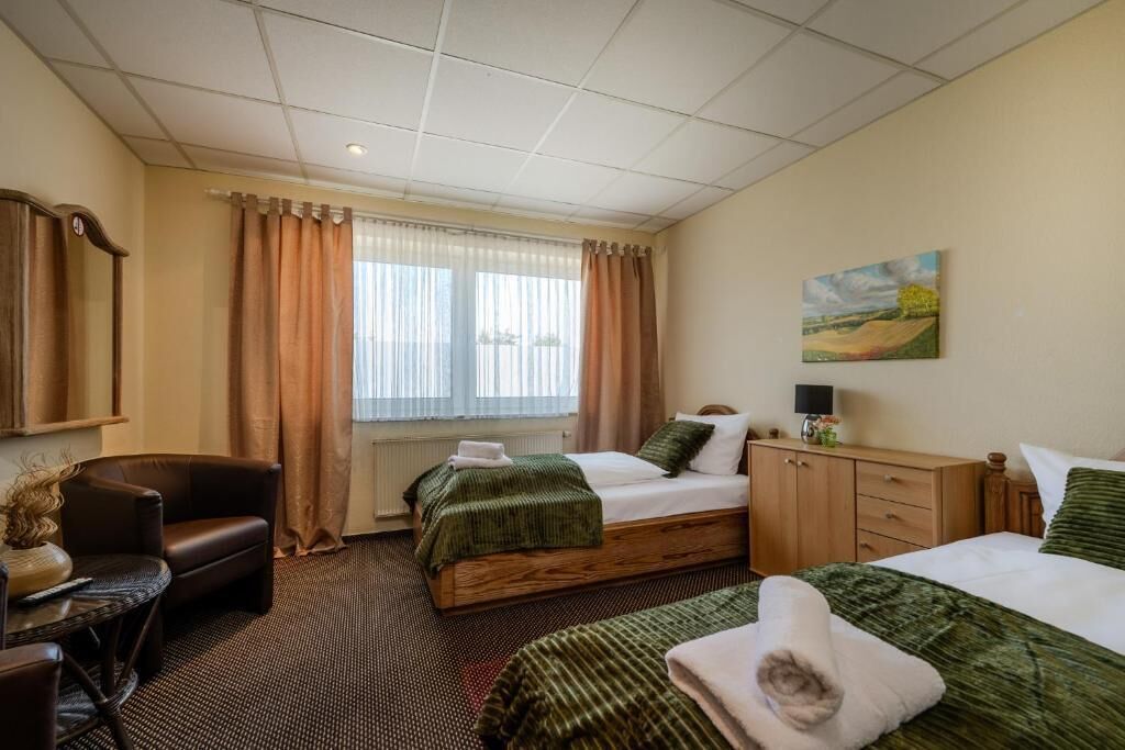 A hotel room with two beds, a desk, a chair, a painting, and a window with curtains.