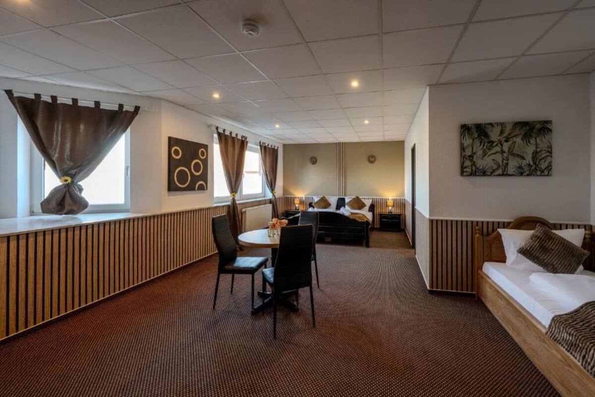 A hotel room with a bed, a sofa, a dining area with chairs, a table, and a window with curtains.