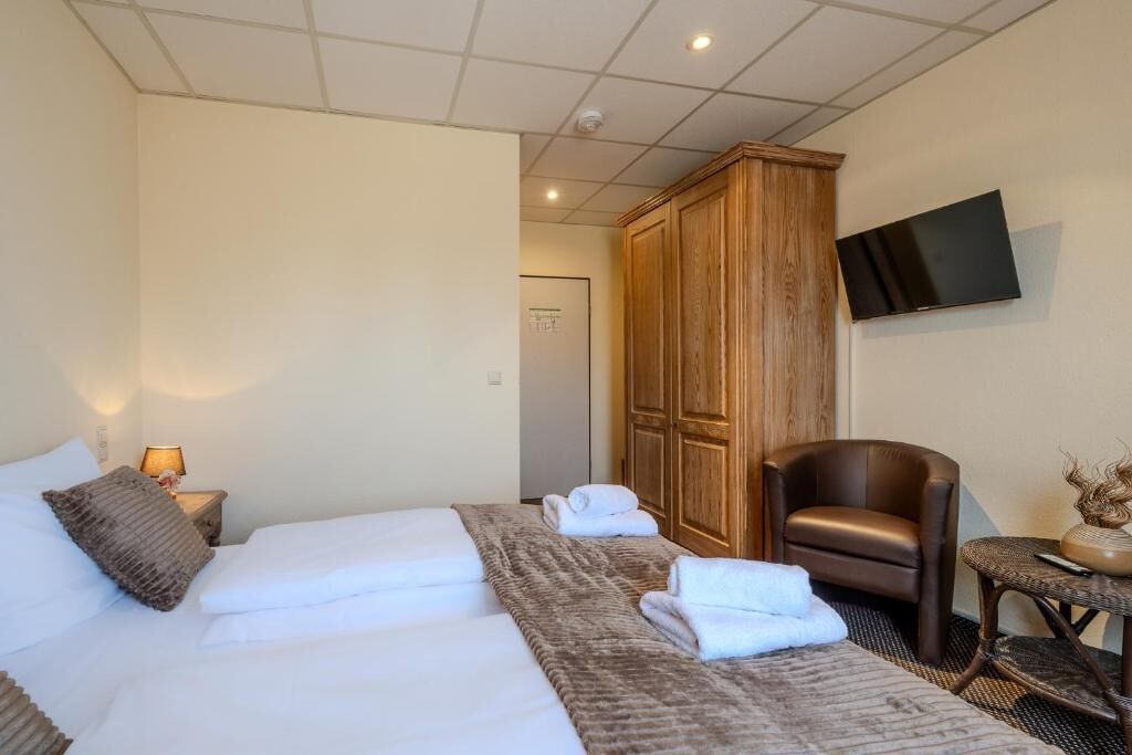 Una camera d'albergo con un letto, un armadio in legno, un televisore a parete e una sedia.