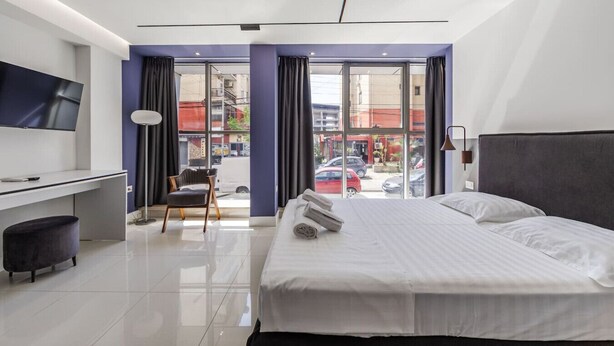 A modern hotel room with a bed, desk, chair, and a TV. - Violet Studio 113 | Love in Colours Collection by PikHost (Durrës)