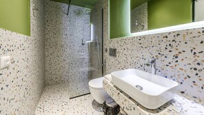 Un baño con ducha, inodoro y lavamanos, con paredes de azulejos veteados y una pared de acento verde.