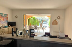 Ein modernes Wohnzimmer mit Fernseher, Dekoration, einem Essbereich mit Außensitzgelegenheiten und Blick auf einen Baum und ein parkendes Auto.